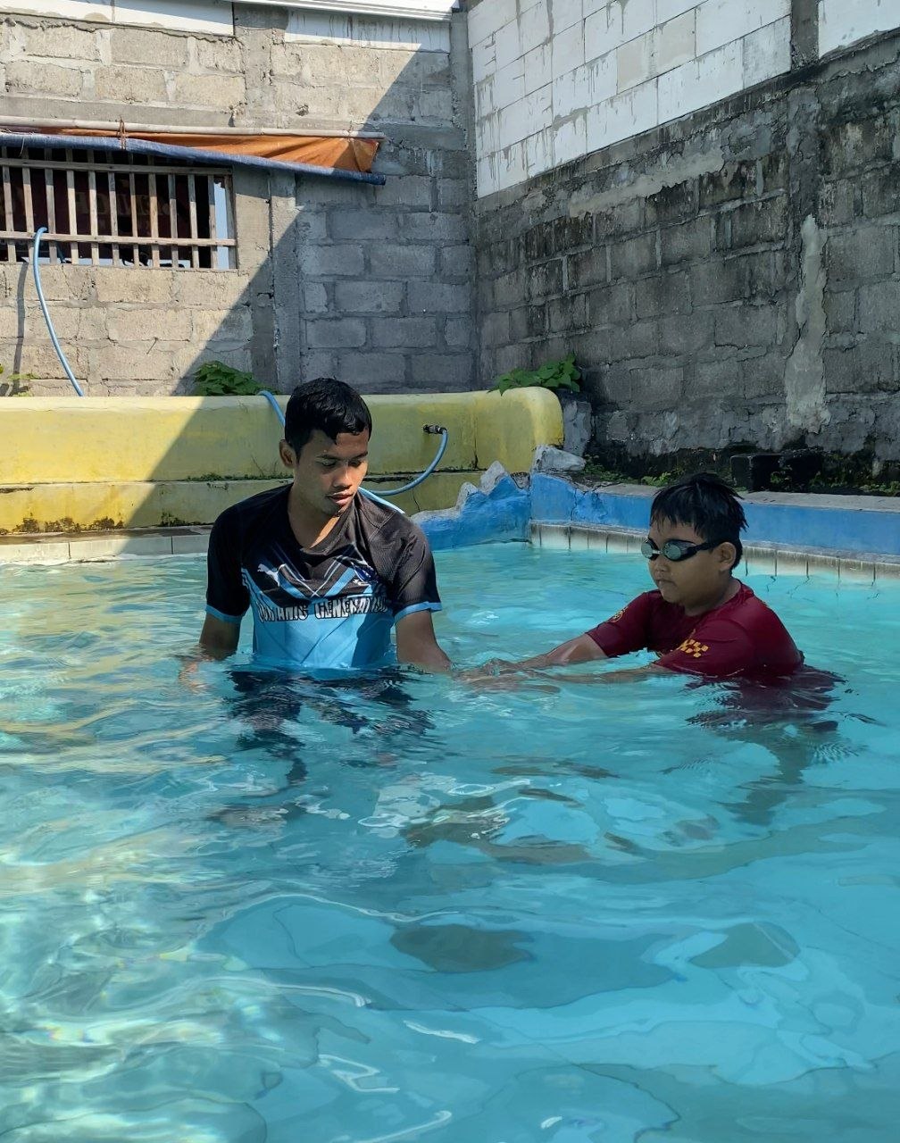 Pelatih Glagah Swim mendampingi seorang anak berlatih di kolam
